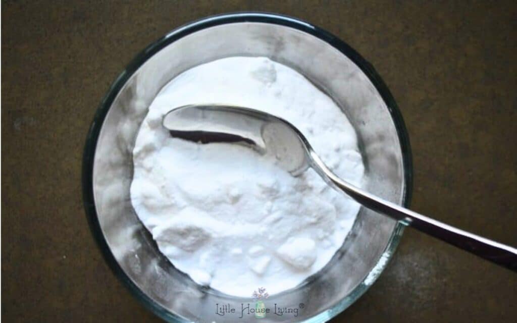Baking soda in a small glass bowl with a spoon and a brown countertop.