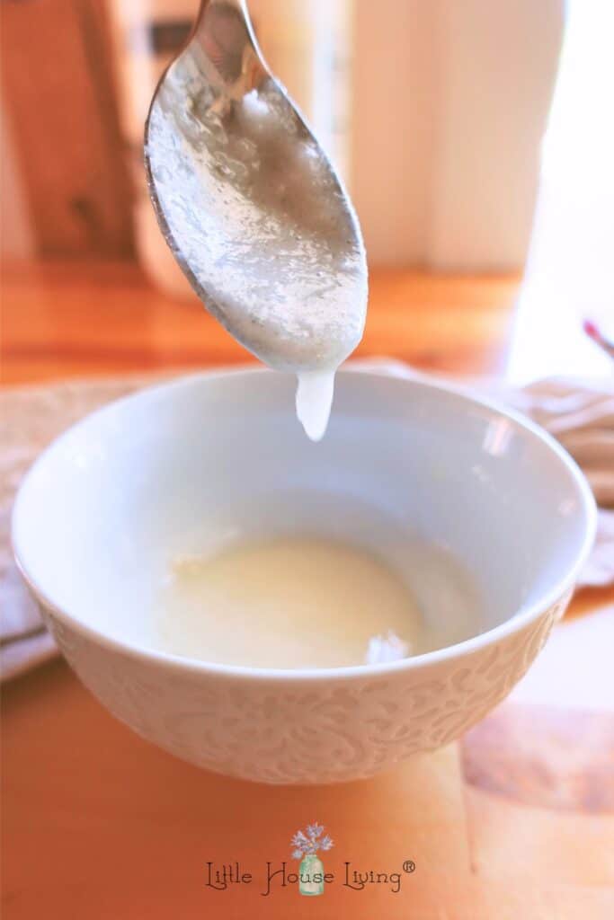 Coconut oil hair mask in a white bowl with a spoon lifting up some product.