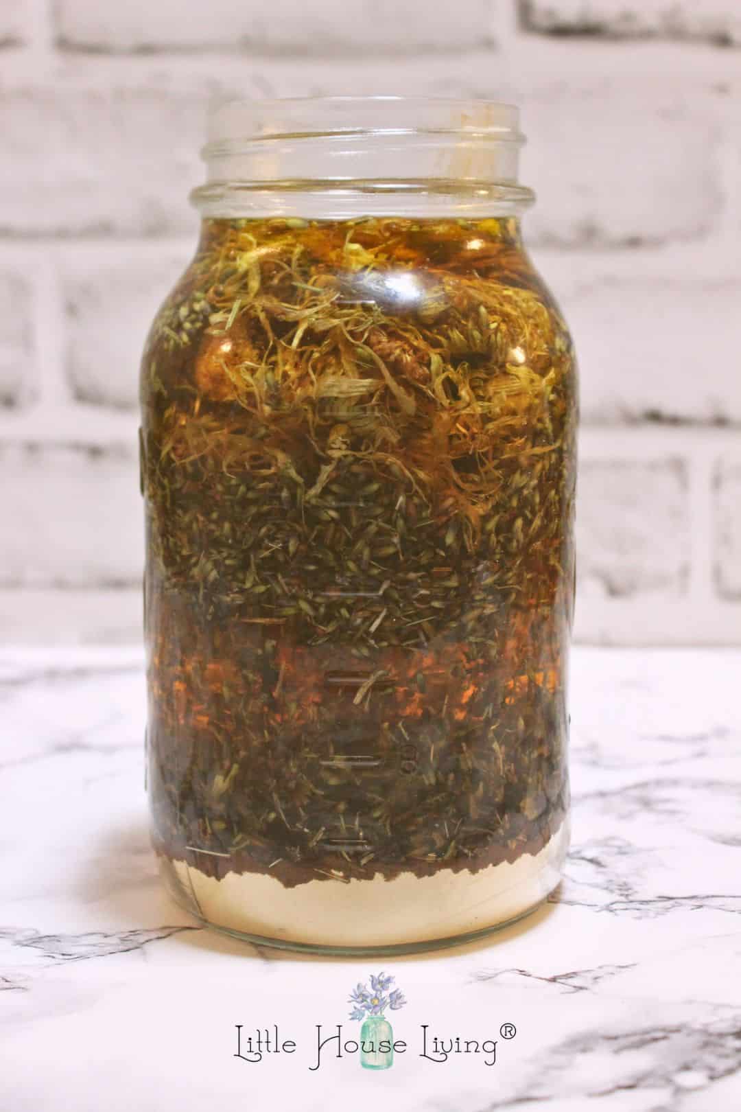 Avocado oil on glass jar with aloe vera powder, comfrey leaves, lavender, and calendula.