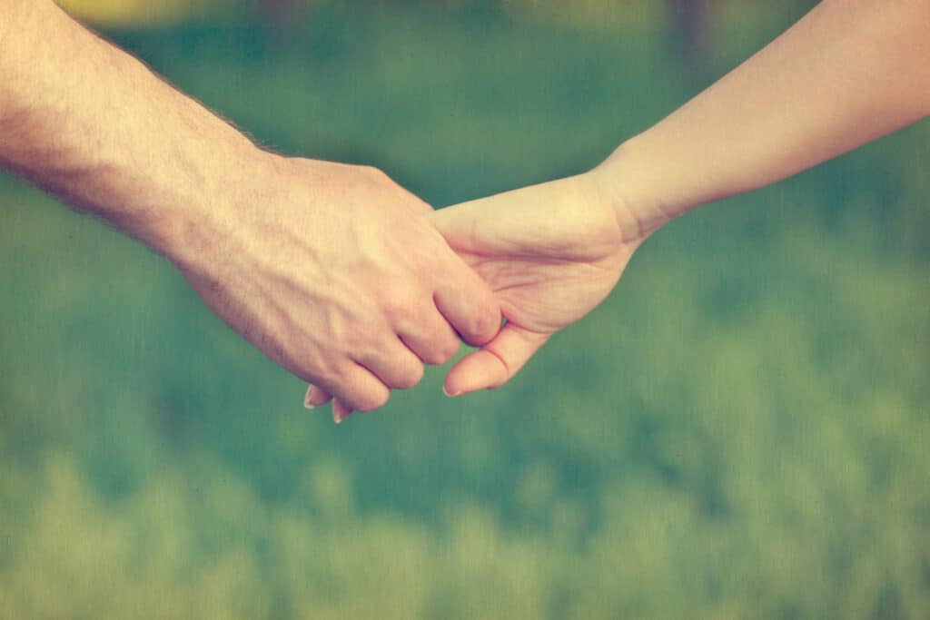 Couple holding hands with a green grass background.
