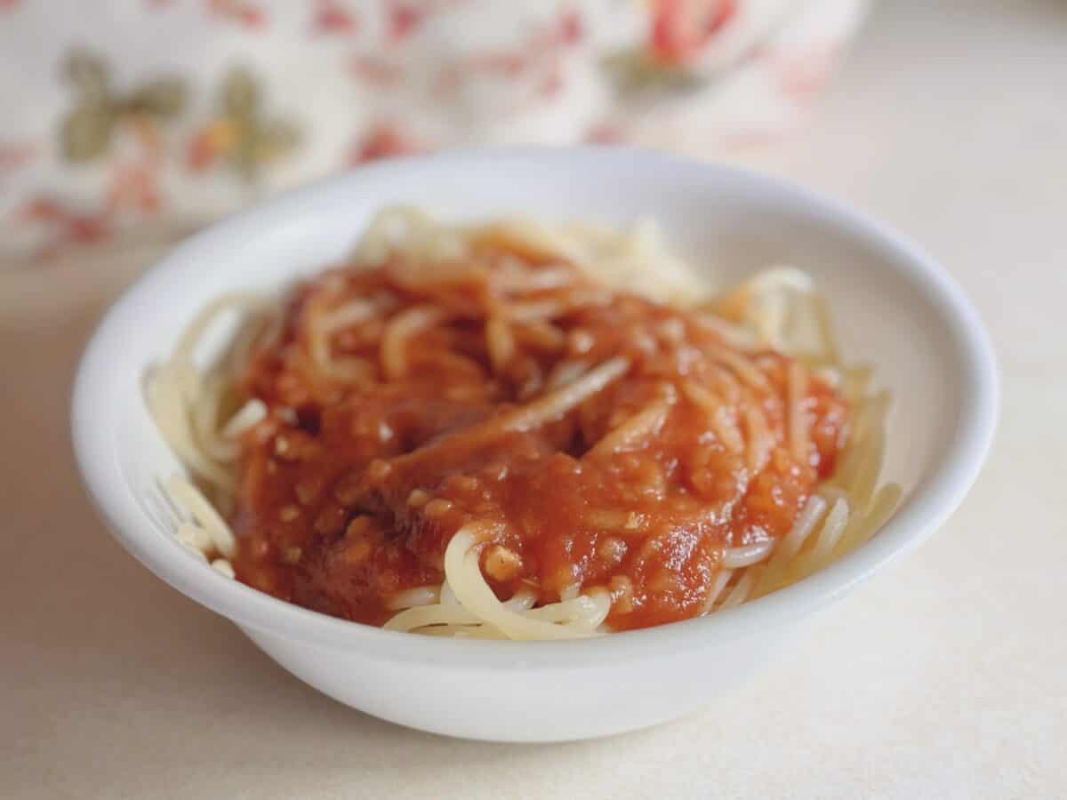 Delicious homemade spaghetti topped with rich tomato sauce in a cozy white bowl. Perfect comfort food for family dinners.