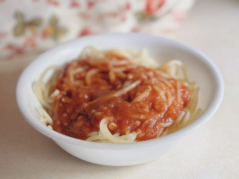 Delicious homemade spaghetti topped with rich tomato sauce in a cozy white bowl. Perfect comfort food for family dinners.